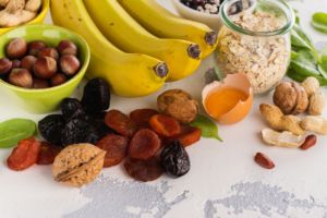 Products rich of potassium - K. Bananas, spinach, nuts, grains, dried fruits overs stone table. Space for text